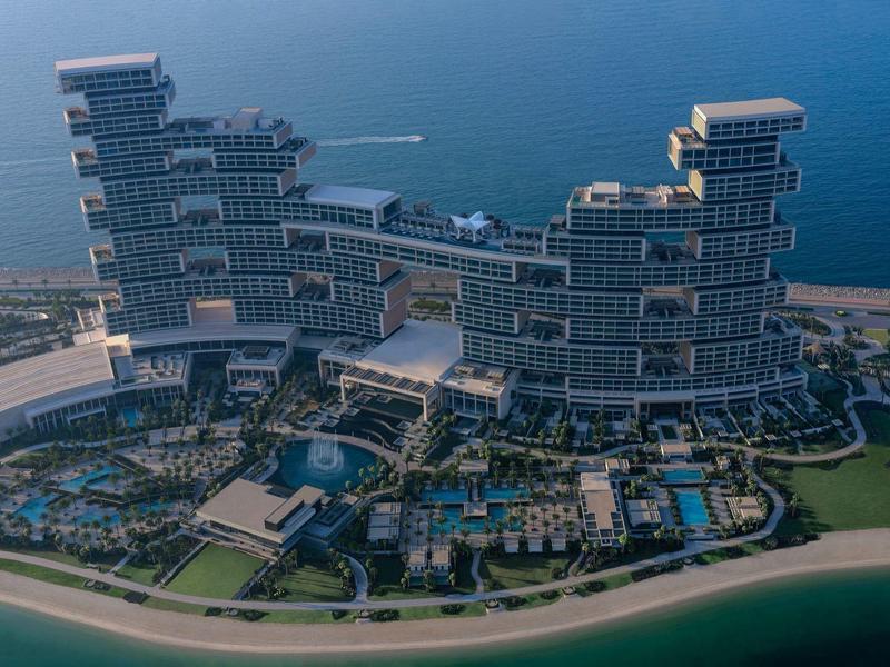 Modernes Hotel mit terrassenförmigen Glasfassaden und mehreren Pools am Strandufer.