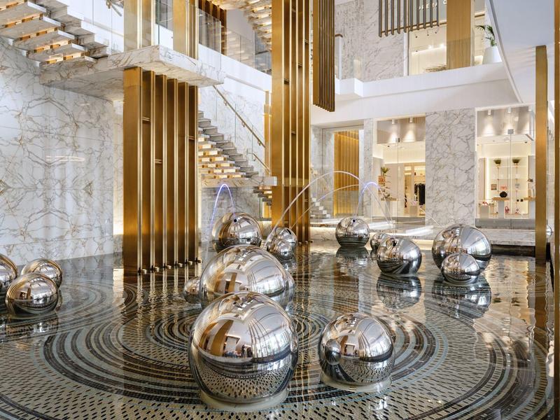 Moderne Lobby mit glänzenden Metallkugeln und Marmorböden, goldenen Säulen und einer Treppe.