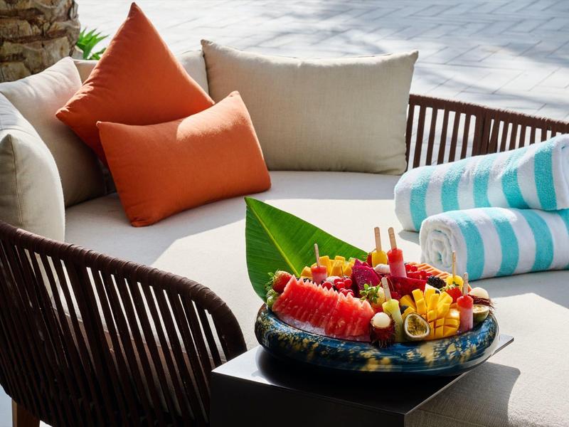 Gemütliche Lounge mit cremefarbener Couch, orangefarbenen Kissen und Teller mit frischem Obst.