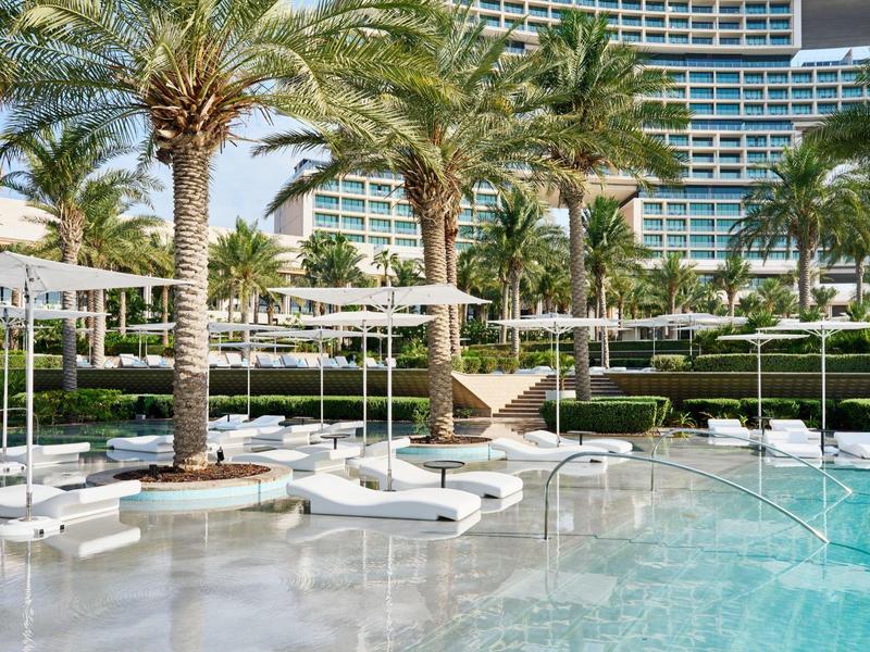 Luxuriöser Poolbereich mit Palmen, weißen Liegen und modernem Hotelgebäude im Hintergrund.