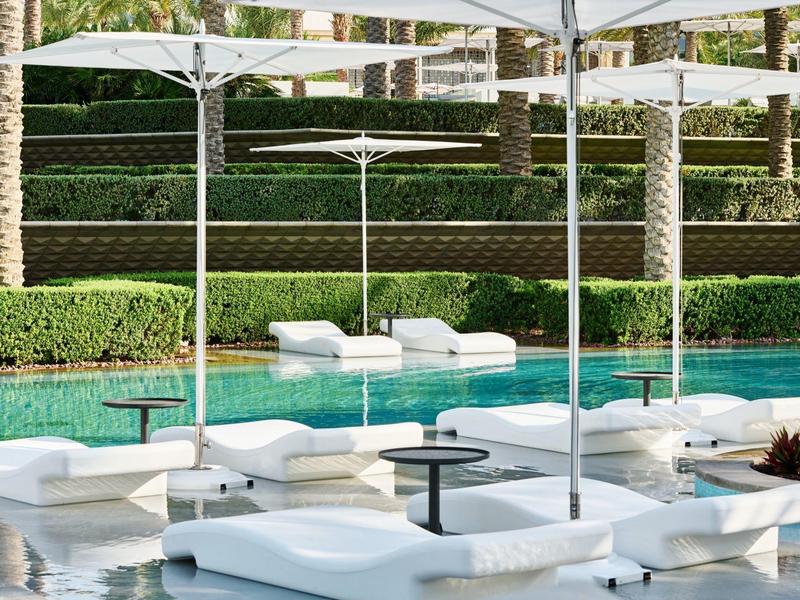 Moderner, klarer Poolbereich mit weißen Liegen, Sonnenschirmen und grünem Garten im Hintergrund.