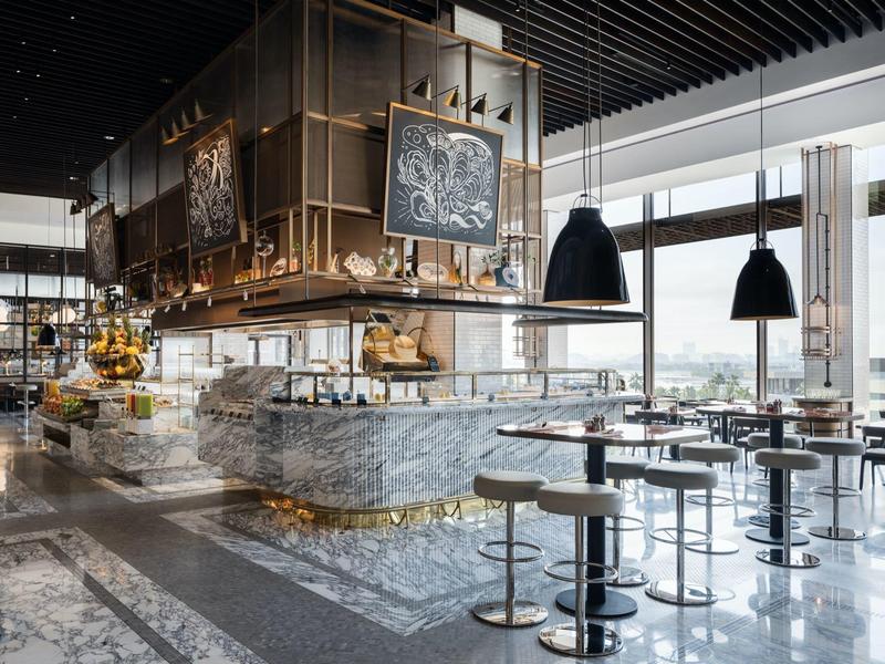 Modernes Café mit Marmor-Theke, hohen Barhockern, schwarzen Lampen und großen Panoramafenstern.