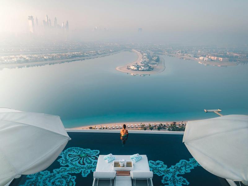 Luxuriöse Dachterrasse mit blauem Teppich, weißen Sitzmöbeln und Blick auf Meer und Stadt im Nebel.
