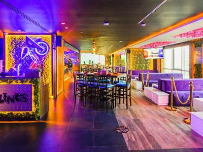 Bright bar with colorful lights, tables, and chairs, modern lively atmosphere.