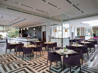 Restaurant moderne avec des tables et chaises élégantes, tapis géométrique et beaucoup de lumière naturelle.