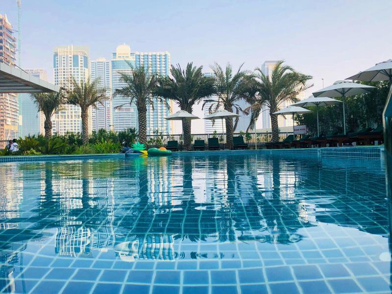 Clear blue swimming pool with palm trees and modern buildings in the background on a sunny day