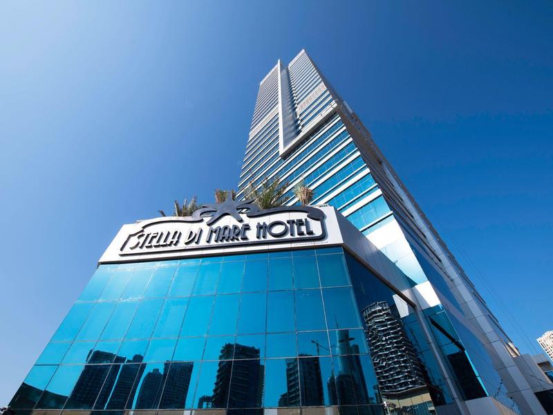 Modern skyscraper with reflective glass facades and hotel sign under a clear blue sky.