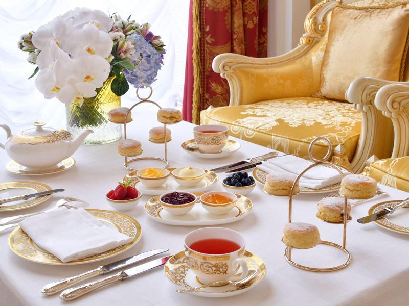 Eleganter Tisch mit Porzellantassen, Gebäck und Blumen in einem luxuriösen Wohnzimmer.