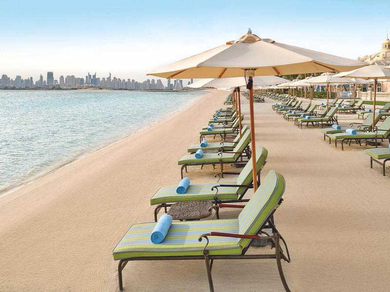 Strand mit Reihen von Liegestühlen, Sonnenschirmen und Blick auf eine Stadt am Horizont.
