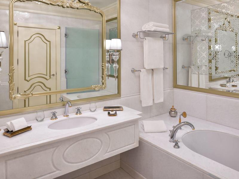 Elegantes Badezimmer mit großer Badewanne, Doppelwaschbecken und goldverzierten Spiegeln.