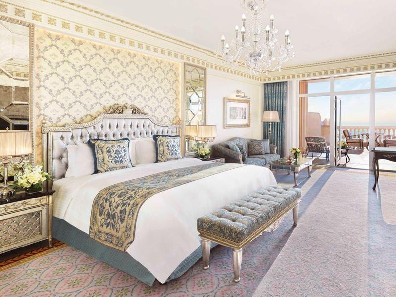 Elegantes, helles Schlafzimmer mit großen Fenstern, großen Betten und feiner goldener Wanddekoration.