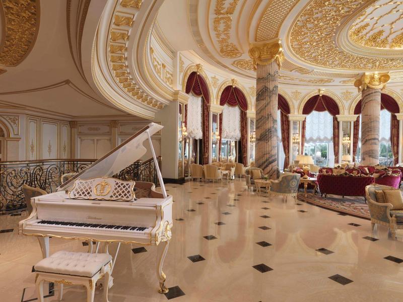 Großer Raum mit weißem Flügelklavier, marmornem Boden, goldverzierten Säulen und luxuriöser Einrichtung.