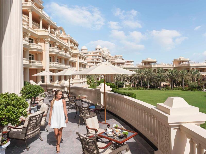Hotelbalkon mit Stühlen, Sonnenschirm und Blick auf gepflegten grünen Rasen bei blauem Himmel.
