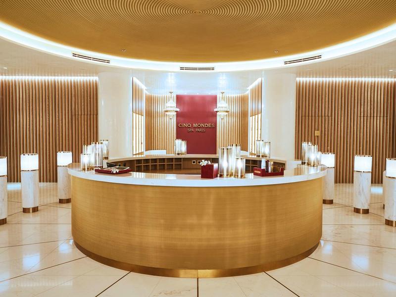 Runder Holztresen in hellem, modern eingerichteten Raum mit kreisrunder Deckenleuchte und weißen Stühlen.