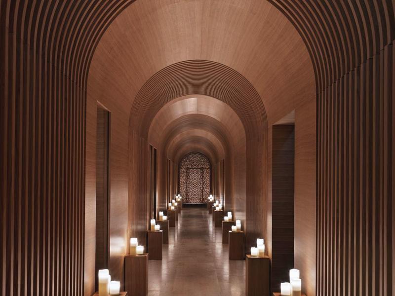 Langer Flur mit braunen, geschwungenen Deckenbögen und sanft leuchtenden Kerzenlampen an den Wänden.