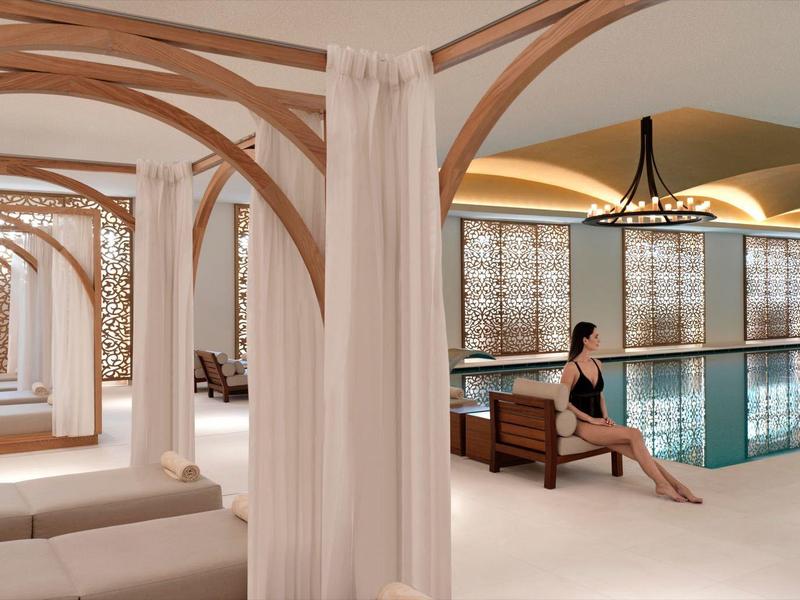 Moderner Wellnessbereich mit Innenpool, Holzbalken, weißen Vorhängen und Liegen in hellem Ambiente.