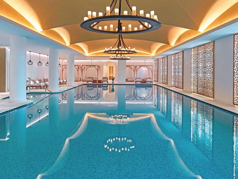 Hallenbad mit klarem Wasser, indirekter Beleuchtung und dekorativen Wandelementen in warmen Farbtönen.