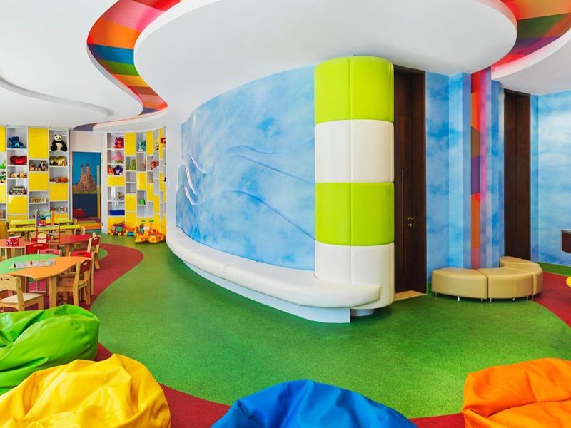Bunter, moderner Spiel- und Lernraum mit weichen Sitzsäcken, Tischen, Stühlen und Wandgestaltung.