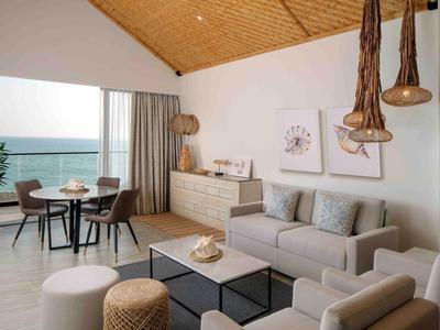 Sala moderna con sofá gris, área de comedor, grandes ventanas y vista al mar.