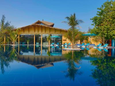Edificio moderno de hotel con fachada de vidrio rodeado de palmeras junto a una piscina tranquila.