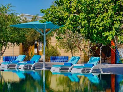 Pool area with blue lounge chairs and umbrella in front of a stone-walled building