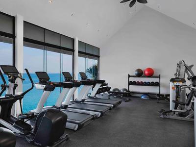 Gym with multiple treadmills and exercise machines with sea view through large windows.