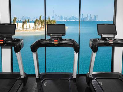 Four treadmills overlooking a pool and city skyline in a hotel gym.