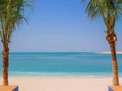Piscina azul entre dos palmeras con vista a la playa de arena blanca y mar turquesa.