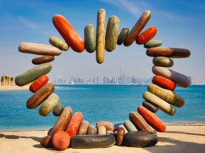 Heart-shaped group of eagle fish buoys on the beach with city and sea in the background.