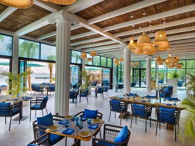 Restaurante luminoso con techo de vigas de madera, sillas azules y mesas preparadas en un hotel tropical.