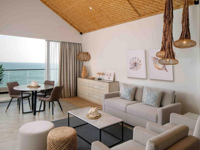 Sala moderna con sofá gris, área de comedor, grandes ventanas y vista al mar.