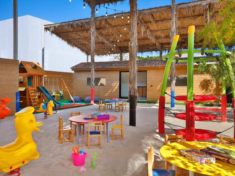 Área de juegos colorida para niños con columpios, toboganes y arenero al aire libre bajo toldo.