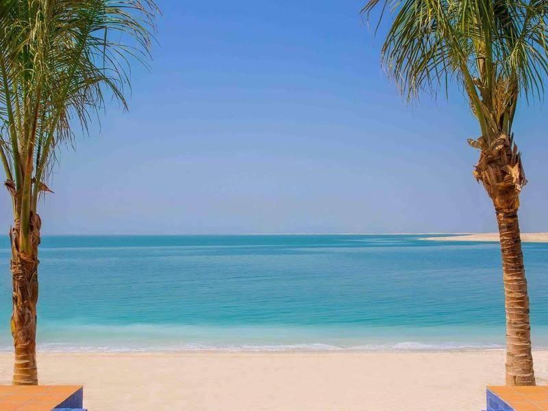 Piscina azul entre dos palmeras con vista a la playa de arena blanca y mar turquesa.