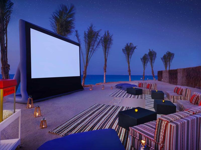 Cine al aire libre en la playa por la noche con asientos y palmeras al fondo.