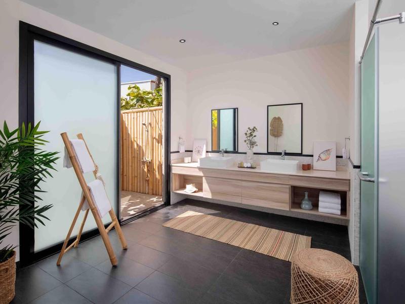 Baño moderno con ventanas de piso a techo, gran espejo y acentos de madera en una habitación de hotel.