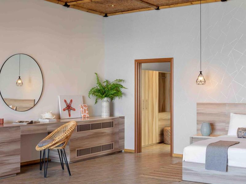 Habitación de hotel moderna con techo de madera, espejo redondo, plantas y cama cómoda.