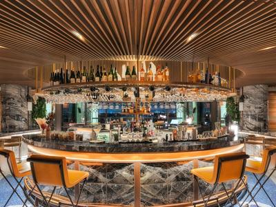 Moderní hotelový bar s kulatým pultem, pohodlnými židlemi a elegantním osvětlením.