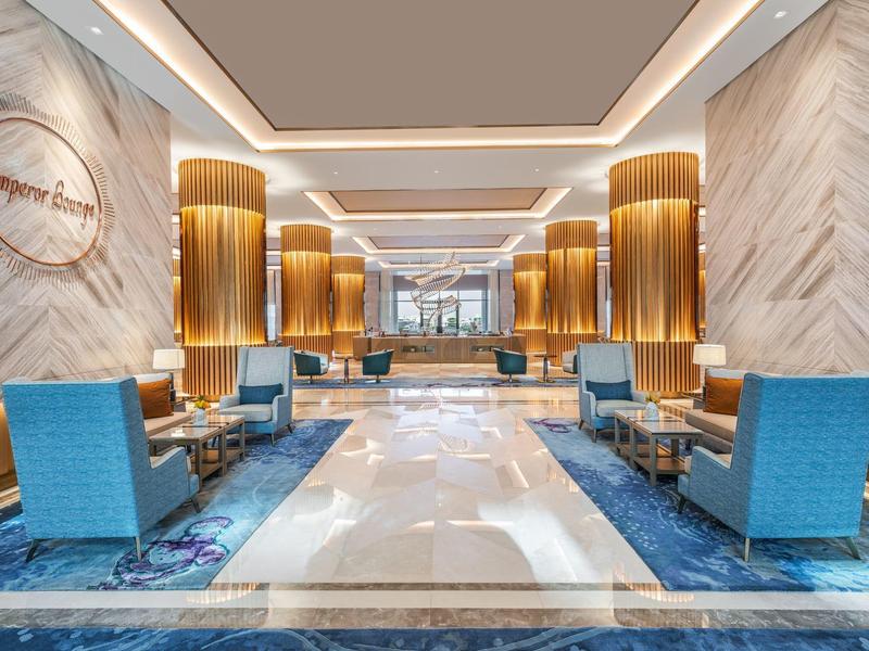 Große moderne Hotellobby mit beigen Wänden, blauen Sesseln, braunen Sitzbänken und Marmorboden.
