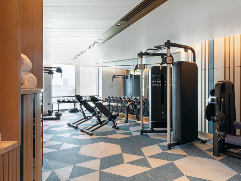 Moderner Fitnessraum mit Geräten, Hanteln, hellen Wänden und geometrischem Bodenmuster.