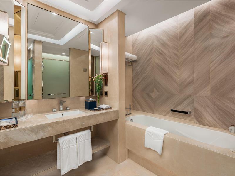 Helles Badezimmer mit Marmorwaschbecken, großer Spiegelwand und Badewanne mit Handtüchern.