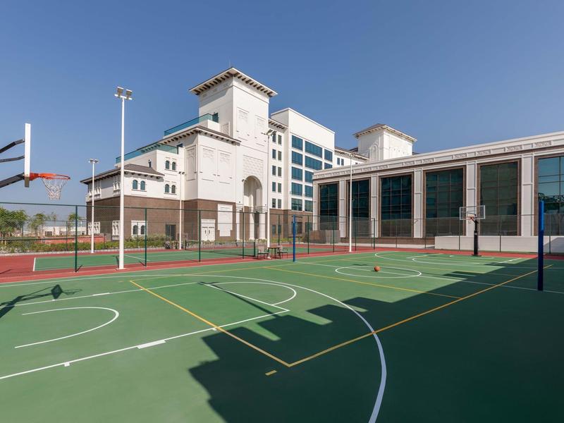 Leerer Basketballplatz mit grünem Boden vor einem großen weißen Gebäude unter blauem Himmel.