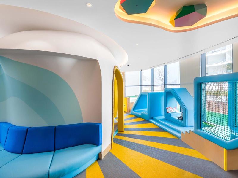 Moderner, bunter Kinderspielraum mit blauen Sitzecken und gelb-blauem Bodenmuster.