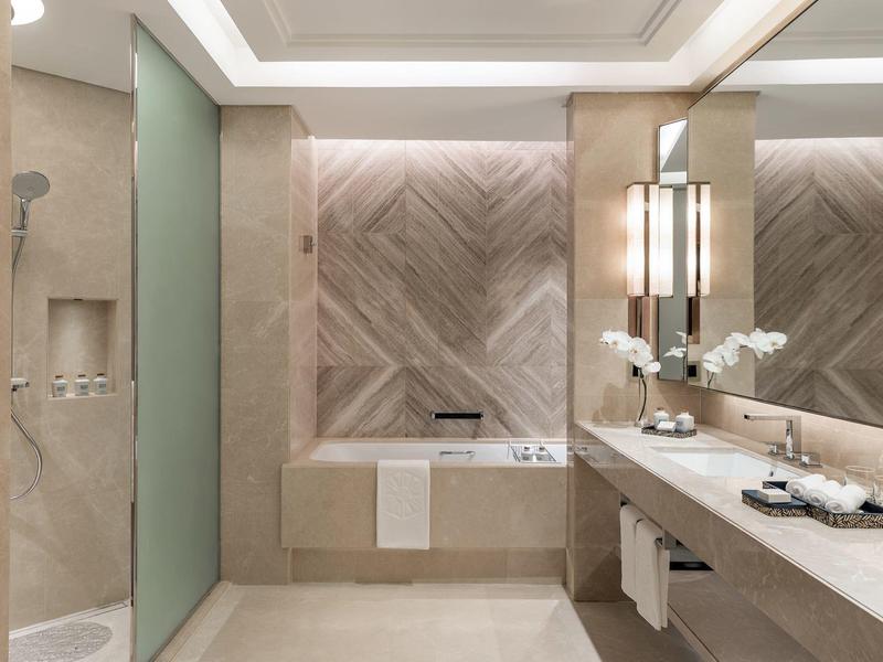 Moderne Badezimmereinrichtung mit großer Badewanne, Dusche, langem Spiegel und hellen Fliesen.