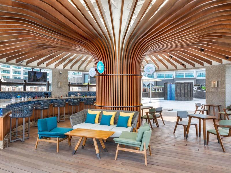 Moderner Lounge-Bereich mit hölzerner Deckenstruktur, bunten Sesseln und minimalistischen Holzmöbeln.