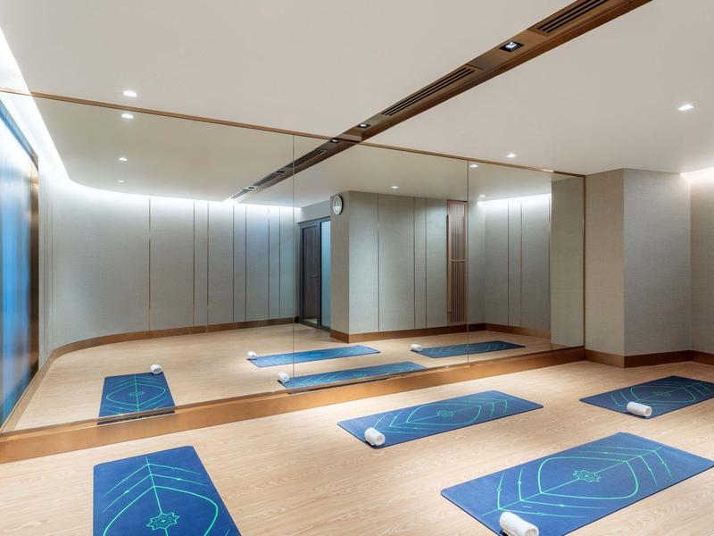 Moderner, heller Raum mit Holzfußboden, großen Spiegeln und blauen Yogamatten.