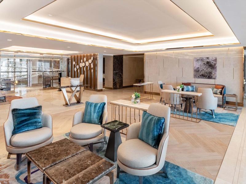 Modern eingerichteter Lounge-Bereich mit Sesseln, Sofas, Teppichen und großem Konferenztisch in hellem Raum.