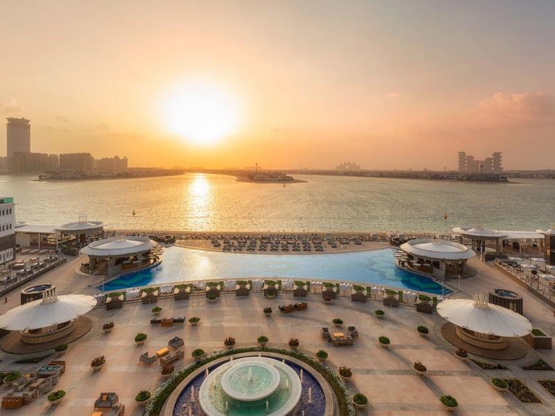Sonnenuntergang über Pool und Terrasse mit Meerblick, Liegestühlen und runden Schirmen.