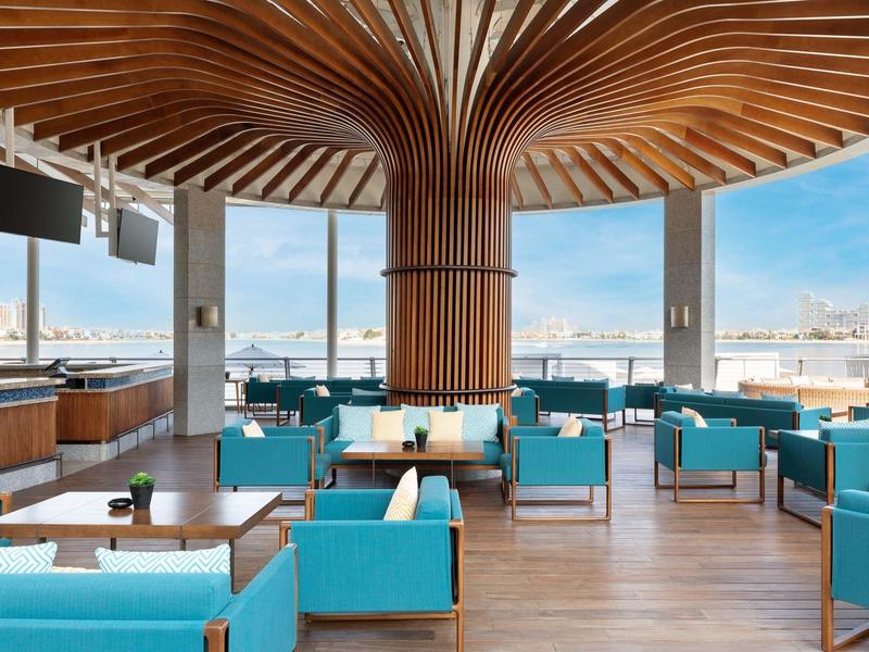 Moderner, heller Raum mit blauen Sesseln, großem Holzsäulendesign und Panoramafenstern mit Stadtblick.