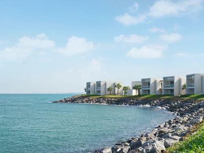 Moderne Gebäude entlang einer felsigen Küste mit grünem Gras und blauem Himmel.