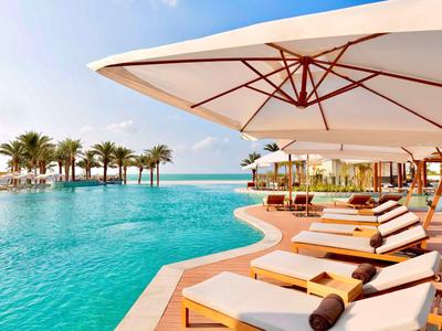 Infinity-Pool mit Sonnenliegen und großen Sonnenschirmen neben Palmen und Meerblick.